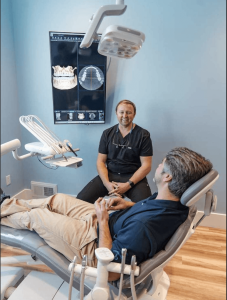 Patient receiving comfortable dental care with dentist in modern Surf City Dental office, featuring dental equipment and educational display on oral health.