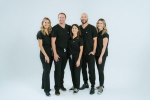 Dental care team at Surf City Dental, dressed in black scrubs, smiling together against a light background, emphasizing family dentistry and commitment to oral health.