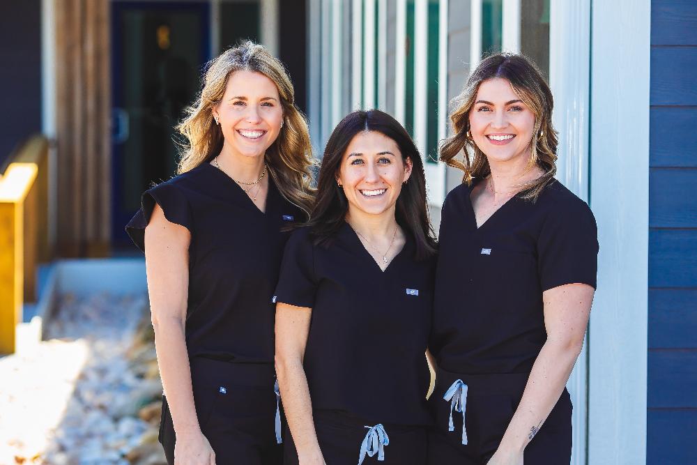 Three dental professionals in black scrubs smiling outside Surf City Dental, emphasizing the practice's focus on patient care and dental implant services.