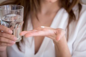 Woman holding a pill in one hand and a glass of water in the other, representing oral conscious sedation dentistry at Surf City Dental for anxiety-free dental care.