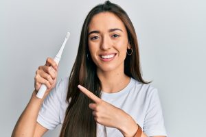 Smiling woman holding an electric toothbrush and pointing to it, representing modern dental gadgets for effective oral health care.