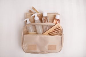 Dental travel kit containing mini toothpaste, folding toothbrush, floss, mouthwash, and comb in a beige case, promoting consistent oral hygiene on the go.